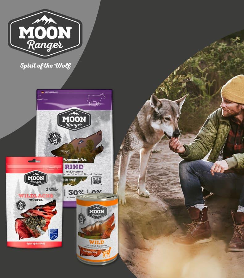 Moon Ranger Hundefutter mit Outdoor‑Szene Moon Ranger Hundefutterprodukte stehen neben einer Szene mit einem Hund, der von einer Person gefüttert wird.