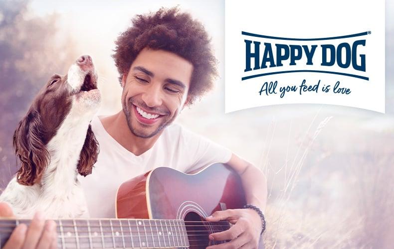 Happy Dog Topbanner Hund neben einem Mann mit einer Gitarre mit großem Happy‑Dog‑Logo im rechten Bildbereich.